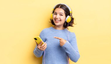 Genç İspanyol kadın heyecanlı ve şaşırmış görünüyor. kulaklıklar ve akıllı telefon konsepti