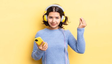 Genç İspanyol kadın kapiş ya da para hareketi yapıyor, sana ödemeni söylüyor. kulaklıklar ve akıllı telefon konsepti