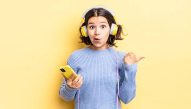 İnançsızlığa şaşırmış genç İspanyol kadın. kulaklıklar ve akıllı telefon konsepti