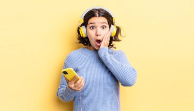 Genç İspanyol kadın şok olmuş ve korkmuş hissediyor. kulaklıklar ve akıllı telefon konsepti