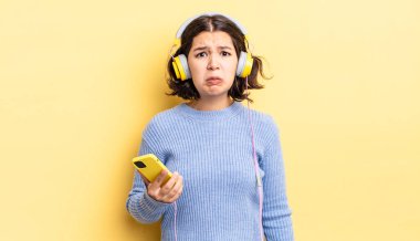 Genç İspanyol kadın üzgün ve mızmızlanıyor. Mutsuz bir bakışı var ve ağlıyor. kulaklıklar ve akıllı telefon konsepti