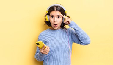 Genç İspanyol kadın şaşırmış görünüyor, yeni bir düşünce, fikir ya da konsept keşfediyor. kulaklıklar ve akıllı telefon konsepti