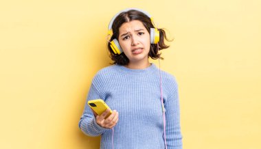 Genç İspanyol kadın şaşkın ve şaşkın hissediyor. kulaklıklar ve akıllı telefon konsepti