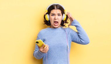 Genç İspanyol kadın ellerini havaya kaldırarak çığlık atıyor. kulaklıklar ve akıllı telefon konsepti