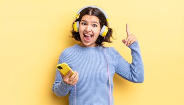 Genç İspanyol kadın bir fikri fark ettikten sonra mutlu ve heyecanlı bir dahi gibi hissediyor. kulaklıklar ve akıllı telefon konsepti