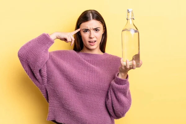 Genç İspanyol kadın şaşkın ve şaşkın hissediyor, senin deli olduğunu gösteriyor. su şişesi kavramı