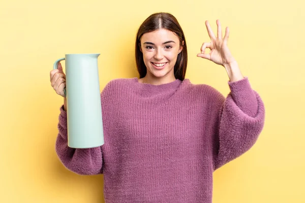 Genç İspanyol kadın kendini mutlu hissediyor, iyi bir jestle onaylıyor. Kahve termosu kavramı