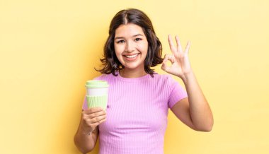 Genç İspanyol kadın kendini mutlu hissediyor, iyi bir jestle onaylıyor. kahve konseptini kaldır.