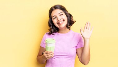 Genç İspanyol kadın mutlu bir şekilde gülümsüyor, el sallıyor, sizi selamlıyor ve selamlıyor. kahve konseptini kaldır.