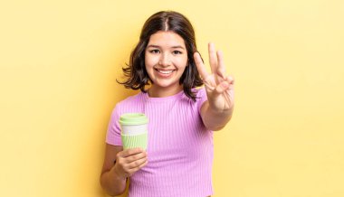 Genç İspanyol kadın gülümsüyor ve arkadaş canlısı görünüyor, üç numarayı gösteriyor. kahve konseptini kaldır.