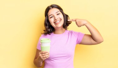 Genç İspanyol kadın kendine güvenerek gülümsüyor ve kendi gülüşünü gösteriyor. kahve konseptini kaldır.