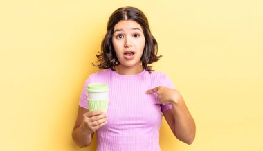 Genç İspanyol kadın şok olmuş ve ağzı açık, kendini işaret ederek şaşırmış görünüyor. kahve konseptini kaldır.