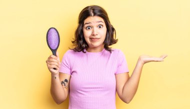 Genç İspanyol kadın şaşkın, şaşkın ve şüpheci hissediyor. saç fırçası konsepti