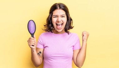 Genç İspanyol kadın şokta, gülüyor ve başarıyı kutluyor. saç fırçası konsepti