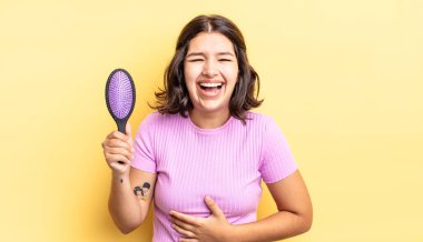 Genç İspanyol kadın komik bir şakaya yüksek sesle gülüyor. saç fırçası konsepti