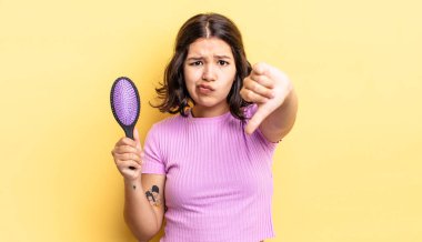 Latin kökenli genç bir kadın kızmış, baş parmağını kaldırmış. saç fırçası konsepti