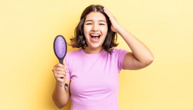 Genç İspanyol kadın mutlu, şaşkın ve şaşırmış görünüyor. saç fırçası konsepti