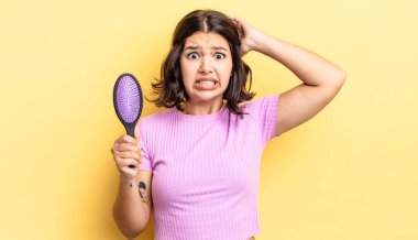 Genç İspanyol kadın stresli, endişeli ya da korkmuş hissediyor, elleri başının üstünde. saç fırçası konsepti