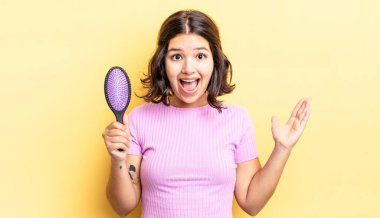 Genç İspanyol kadın kendini mutlu hissediyor ve inanılmaz bir şeye hayret ediyor. saç fırçası konsepti