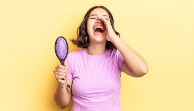 Genç İspanyol kadın kendini mutlu hissediyor, elleri ağzının kenarında bağırıyor. saç fırçası konsepti