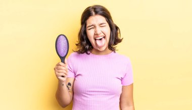 Neşeli ve asi tavırları olan, şaka yapan ve dilini dışarı çıkaran genç İspanyol bir kadın. saç fırçası konsepti