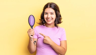 Genç İspanyol kadın neşeyle gülümsüyor, mutlu hissediyor ve bir tarafı işaret ediyor. saç fırçası konsepti