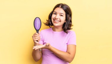 Genç İspanyol kadın neşeyle gülümsüyor, mutlu hissediyor ve bir konsept gösteriyor. saç fırçası konsepti