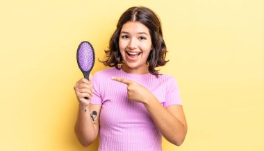 Genç İspanyol kadın heyecanlı ve şaşırmış görünüyor. saç fırçası konsepti