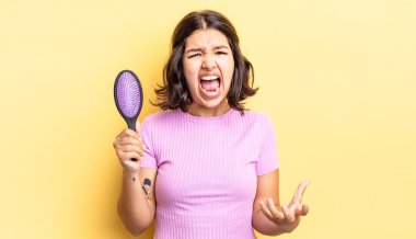 Genç İspanyol kadın kızgın, sinirli ve hayal kırıklığına uğramış görünüyor. saç fırçası konsepti