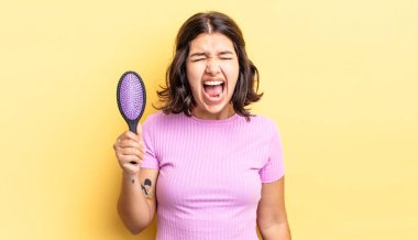 Genç İspanyol kadın agresif bir şekilde bağırıyor, çok kızgın görünüyor. saç fırçası konsepti