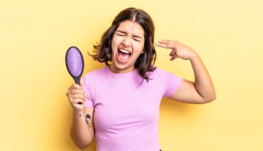 Genç İspanyol kadın mutsuz ve stresli görünüyor, intihar jesti silah işareti yapıyor. saç fırçası konsepti