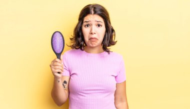 Genç İspanyol kadın üzgün ve mızmızlanıyor. Mutsuz bir bakışı var ve ağlıyor. saç fırçası konsepti