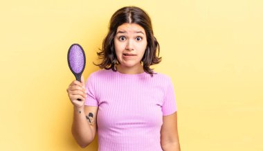 Genç İspanyol kadın şaşkın ve şaşkın görünüyor. saç fırçası konsepti