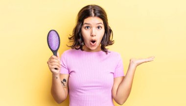 Genç İspanyol kadın şaşırmış ve şok olmuş görünüyor. Çenesi düşmüş ve elinde bir nesne tutuyor. saç fırçası konsepti