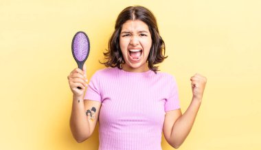 Genç İspanyol kadın öfkeli bir ifadeyle agresif bir şekilde bağırıyor. saç fırçası konsepti