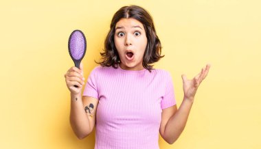 Genç İspanyol kadın şok olmuş ve şaşırmış hissediyor. saç fırçası konsepti