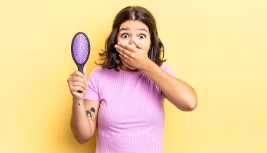 Genç İspanyol kadın şok olmuş ellerle ağzını kapatıyor. saç fırçası konsepti