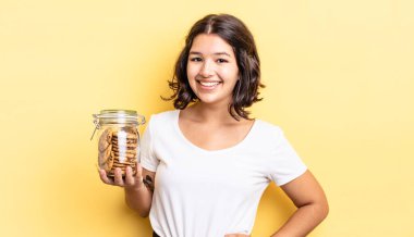 Genç İspanyol kadın mutlu bir şekilde gülümsüyor, eli kalçasında ve kendinden emin. kurabiye şişesi konsepti