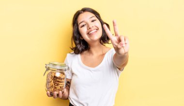 Genç İspanyol kadın gülümsüyor ve mutlu görünüyor, zafer ya da barış işareti yapıyor. kurabiye şişesi konsepti