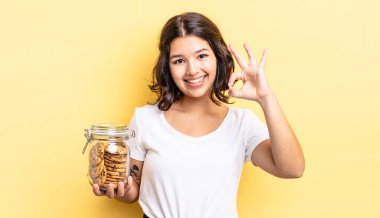 Genç İspanyol kadın kendini mutlu hissediyor, iyi bir jestle onaylıyor. kurabiye şişesi konsepti