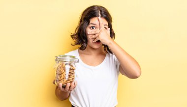 Genç İspanyol bir kadın şok olmuş, korkmuş ya da korkmuş görünüyor. Yüzü elle kapatılmış. kurabiye şişesi konsepti