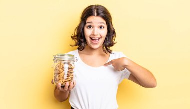 Genç İspanyol kadın kendini mutlu hissediyor ve heyecanla kendini işaret ediyor. kurabiye şişesi konsepti