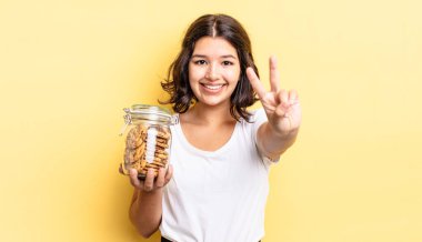 Genç İspanyol kadın gülümsüyor ve arkadaş canlısı görünüyor, iki numarayı gösteriyor. kurabiye şişesi konsepti