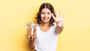 Genç İspanyol kadın gülümsüyor ve arkadaş canlısı görünüyor, dört numarayı gösteriyor. kurabiye şişesi konsepti