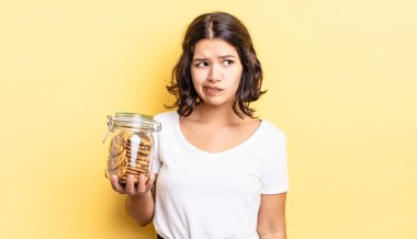 Genç İspanyol kadın üzgün, üzgün ya da kızgın hissediyor ve yana bakıyor. kurabiye şişesi konsepti