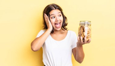 Genç İspanyol kadın mutlu, heyecanlı ve şaşırmış hissediyor. kurabiye şişesi konsepti