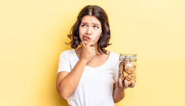 Genç İspanyol kadın düşünüyor, kuşkulu ve şaşkın hissediyor. kurabiye şişesi konsepti