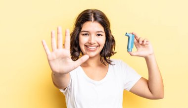 Genç İspanyol kadın gülümsüyor ve arkadaş canlısı görünüyor, beş numarayı gösteriyor. astım konsepti