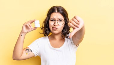 Latin kökenli genç bir kadın kızmış, baş parmağını kaldırmış. hastalık hapları konsepti