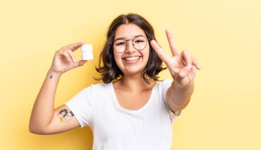 Genç İspanyol kadın gülümsüyor ve mutlu görünüyor, zafer ya da barış işareti yapıyor. hastalık hapları konsepti